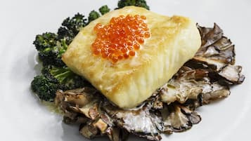 Une assiette contenant un morceau de poisson garni de caviar rouge, accompagné de brocolis et de champignons.