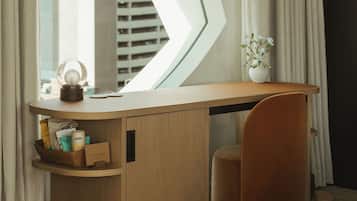 A modern hotel room with a large window, a wooden desk, a small chair, and a lamp.
