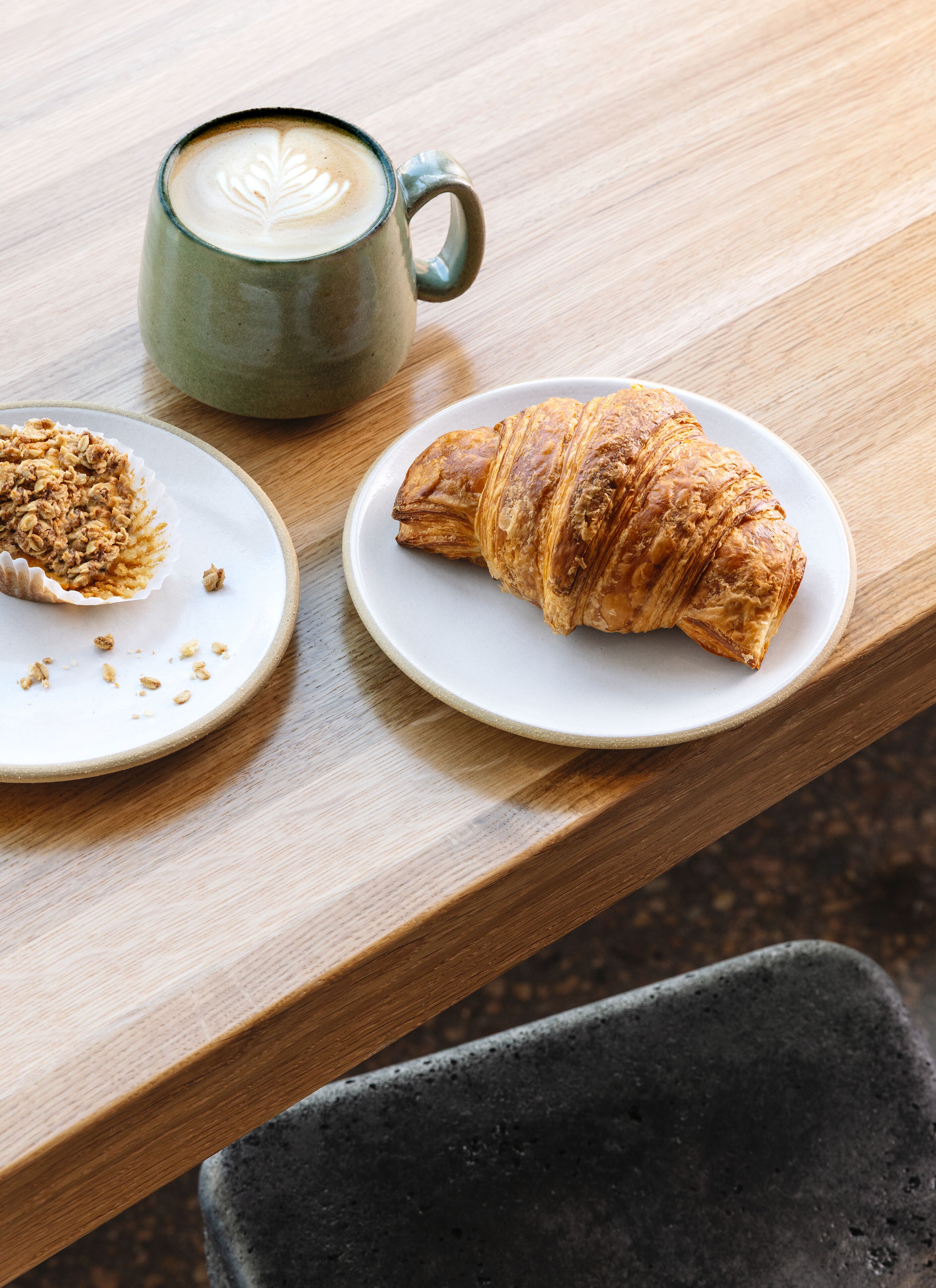 Una mesa de madera con un croissant y una taza de café sobre platos blancos.