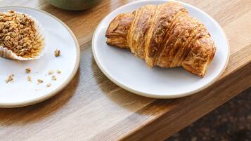 Una mesa de madera con un croissant y una taza de café sobre platos blancos.