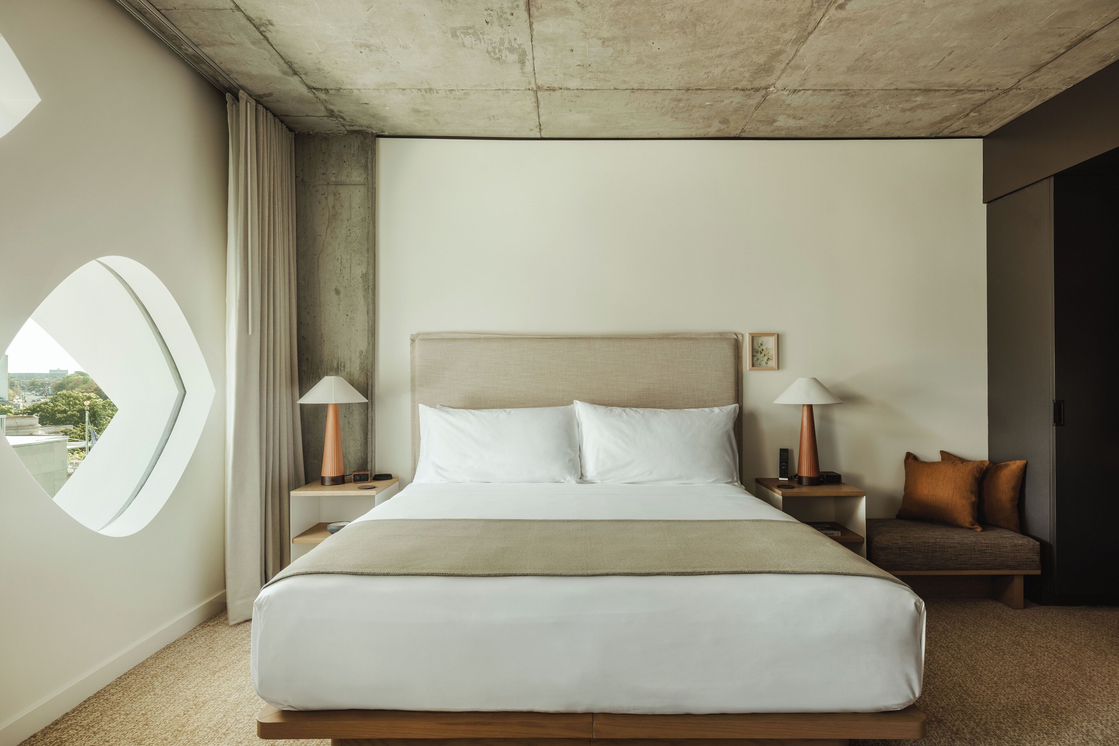 A hotel room with a large bed, two bedside tables, a nightstand, a view of the outdoors, and a modern design.
