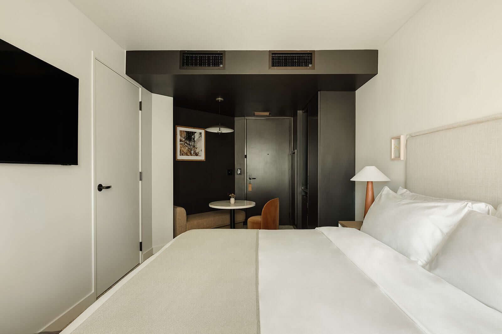 A hotel room with a large bed, a desk, a chair, a small table, and a TV mounted on the wall.