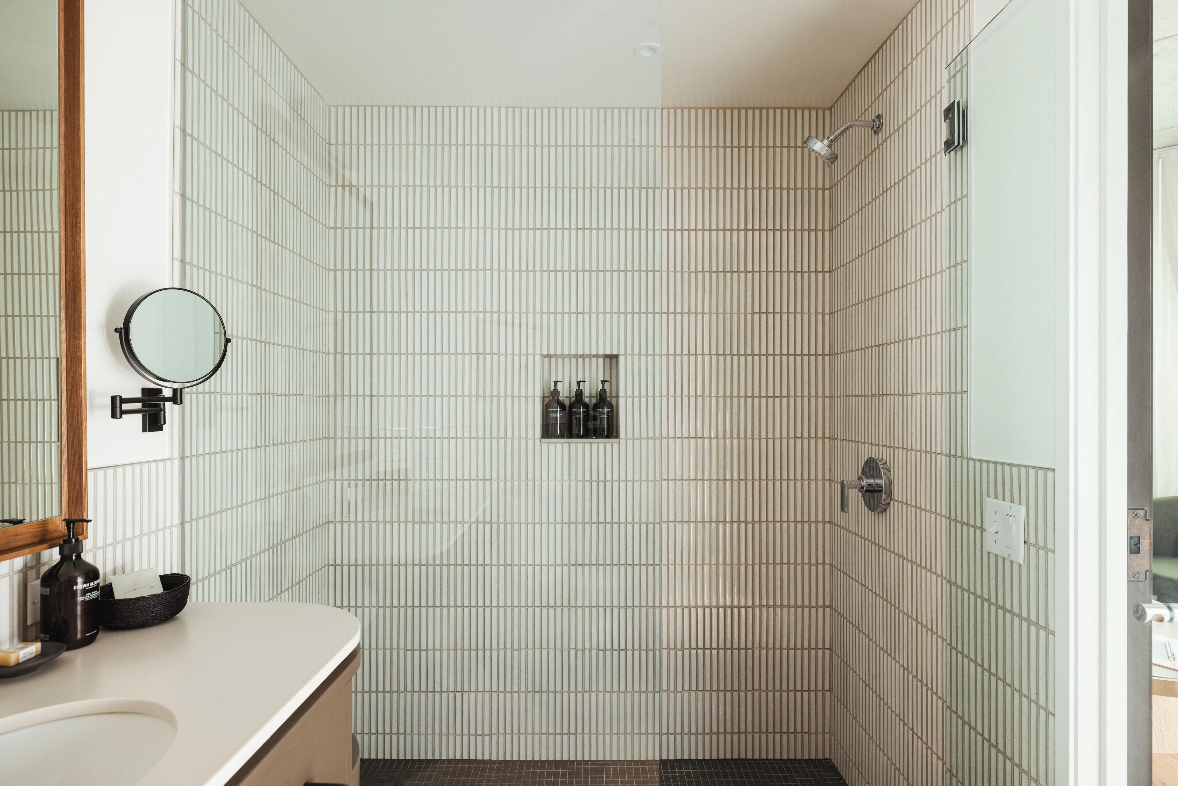 A bathroom with a sink, mirror, and a shower area with a tiled wall.
