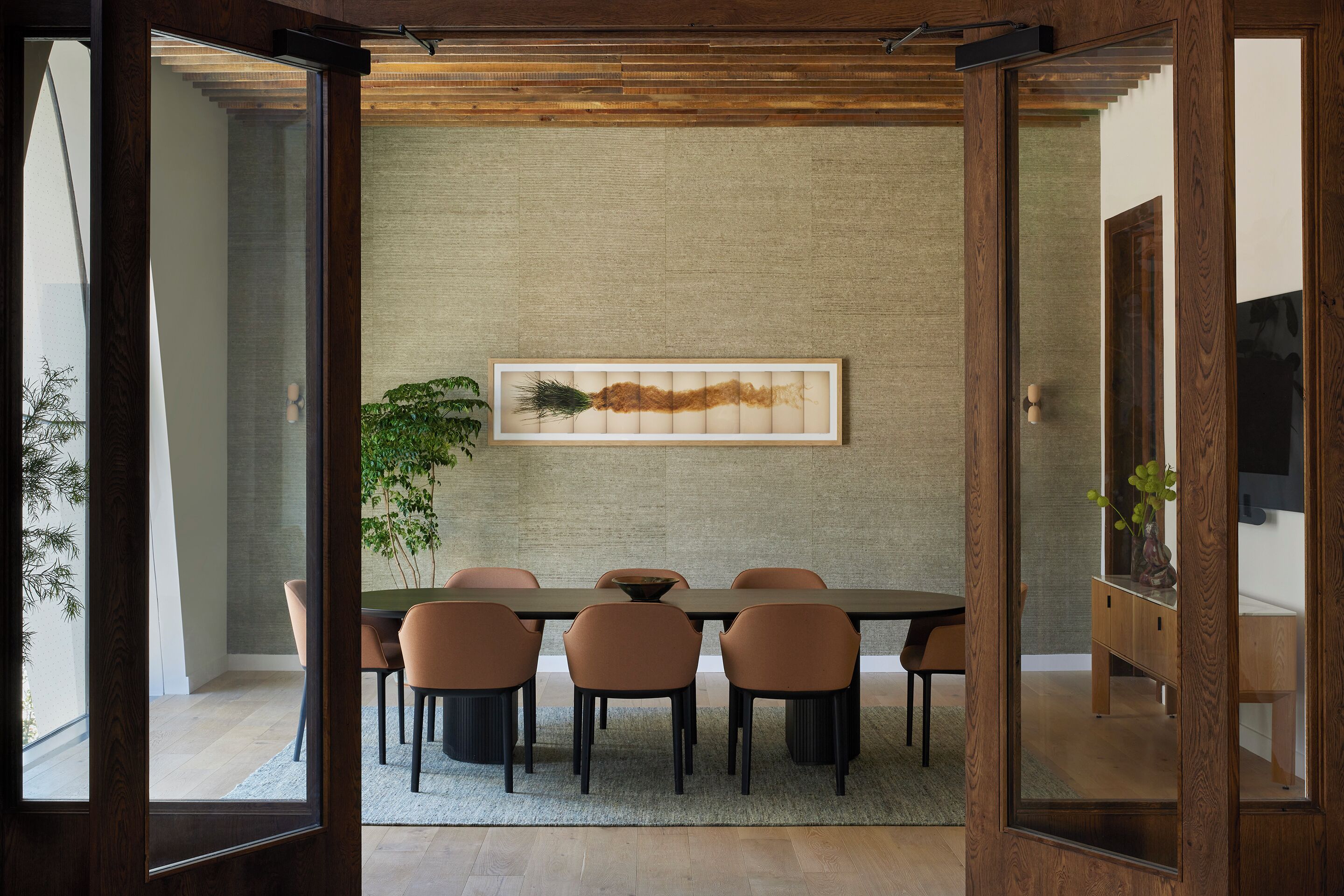 A dining area with a long table, six chairs, and a large painting on the wall.