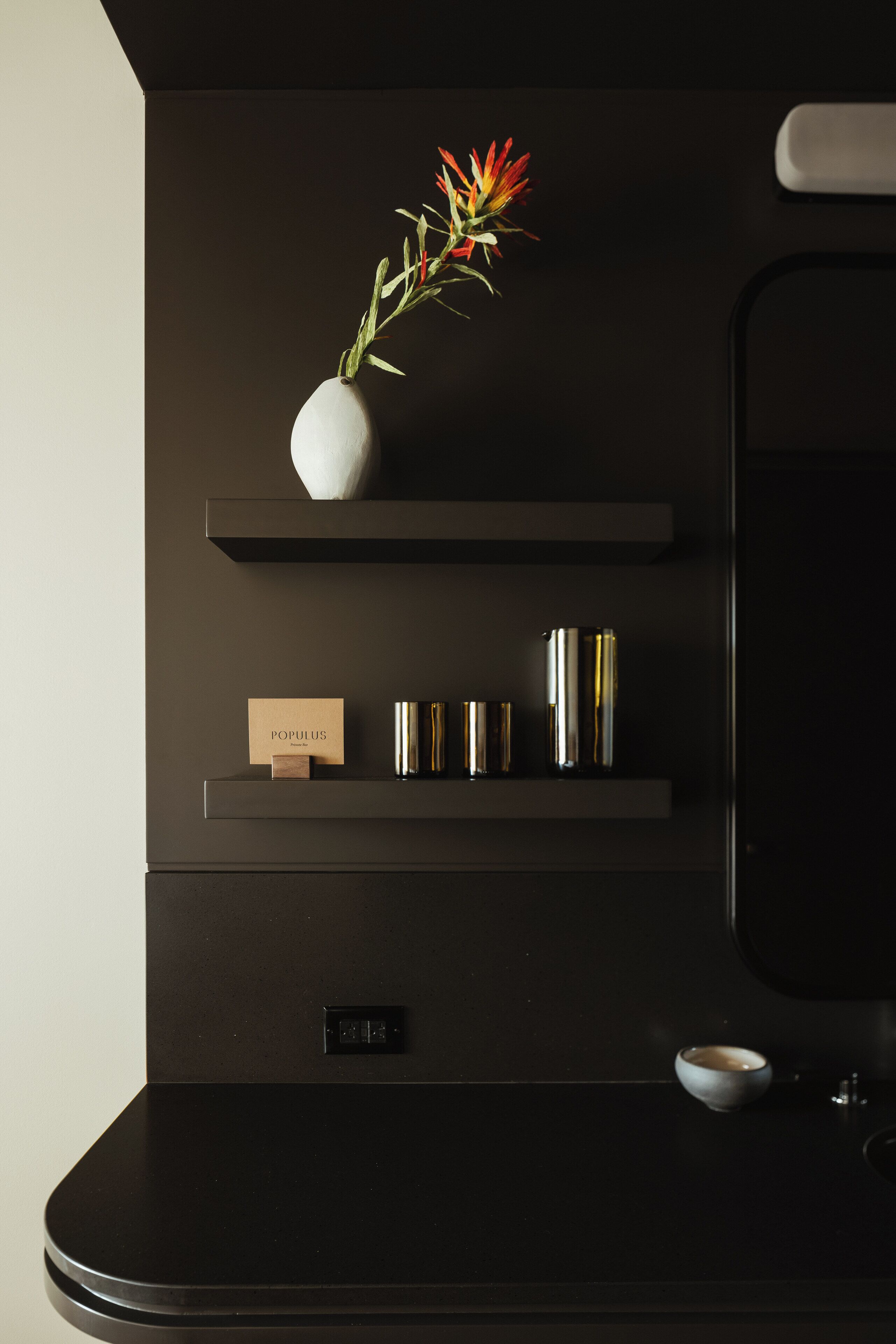 A modern bathroom with a dark theme, a vase with flowers, and a mirror.