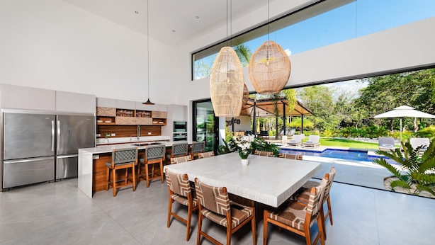 A modern kitchen with a large island, stainless steel appliances, and a dining area with a view of a swimming pool and garden. - Beachside Bliss 4BR Lux Villa, Pool, Terrace, Golf (Pinilla)