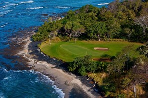 An aerial view of a golf course with a sandy beach and ocean on one side, surrounded by dense trees. - Beachside Bliss 4BR Lux Villa, Pool, Terrace, Golf (Pinilla)