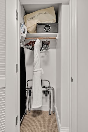 A bathroom with a white towel hanging on a rack, a shower chair, and a towel rack with various towels.