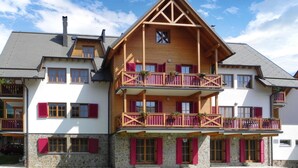 A multi-story building with a steeply pitched roof, wooden balconies with red shutters, and stone accents around the windows. - Stunning apartment in Pohorje with WiFi (Pohorje)