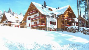 A multi-story chalet with wooden balconies and a snow-covered roof, surrounded by trees. - Stunning apartment in Pohorje with WiFi (Pohorje)