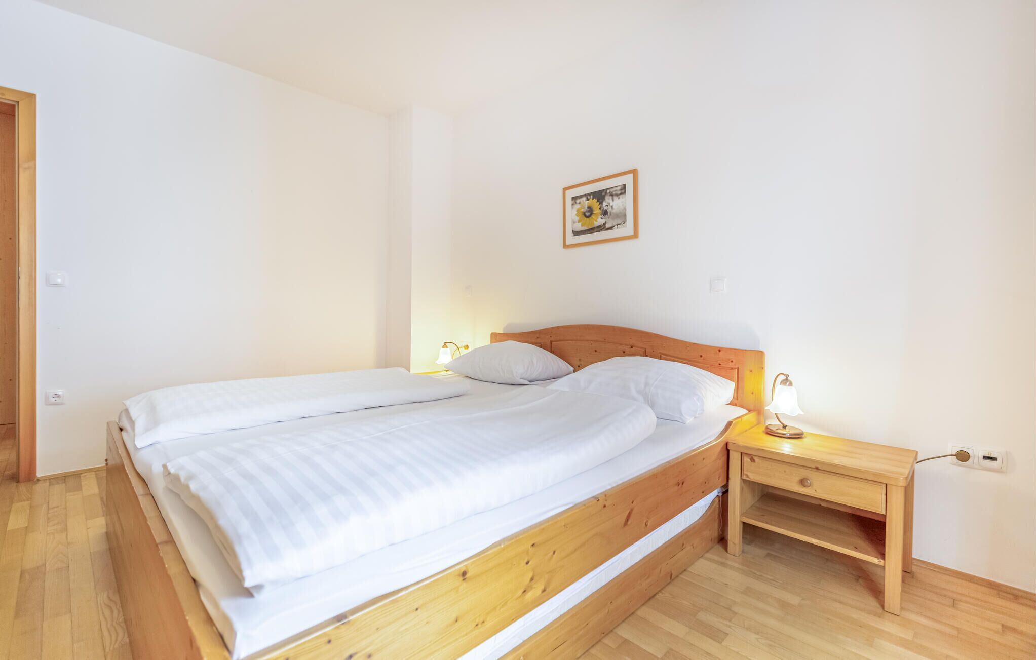 A single-bed room with a wooden headboard, a bedside table with a lamp, and a small shelf.