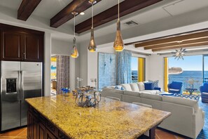 A modern kitchen with a granite countertop, stainless steel refrigerator, and pendant lighting.