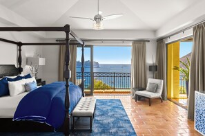 Un lit à baldaquin avec vue sur la mer, un balcon avec un fauteuil et une grande fenêtre avec des rideaux.