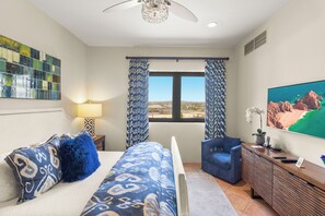 A bedroom with a bed, a desk, a chair, a TV, and a view of a coastal landscape.