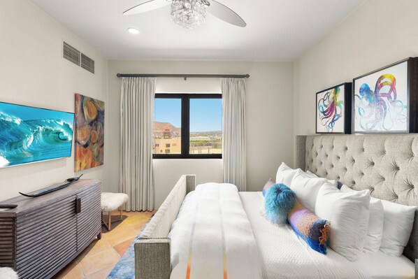 A hotel room with a bed, a TV, artwork, and a view of the city.