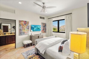 Un dormitorio con cama, tocador, espejo, obras de arte y ventana con vistas.