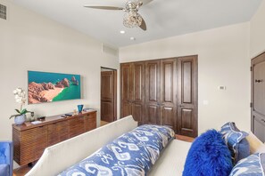 Une chambre à coucher avec un lit, un bureau orné d’un vase et de télécommandes, un ventilateur de plafond et une grande armoire en bois.