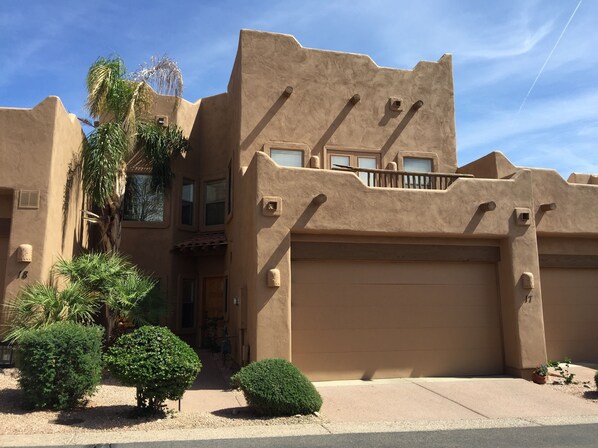 A building with a stucco exterior, multiple windows, and a garage. There are several green shrubs in the front yard.