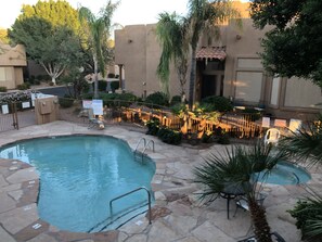 A swimming pool area with stone tiles, palm trees, and a fenced garden.