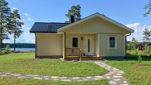 Ein kleines, eingeschossiges Gebäude mit einem geneigten Dach, einer Veranda mit Holzgeländer und einem kleinen Fenster auf der rechten Seite.