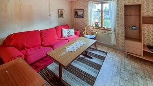A living room with a red sofa, a wooden coffee table, a wicker chair, a window with curtains, and a wooden cabinet.