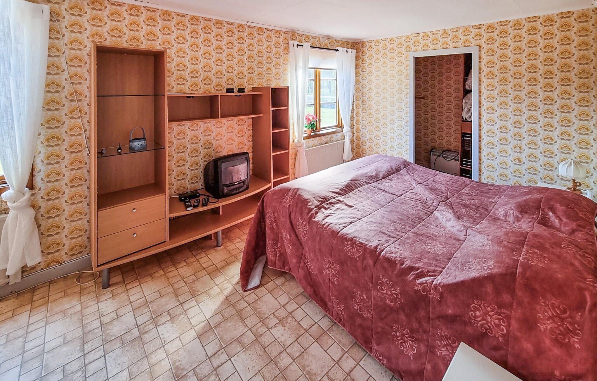 Un dormitorio con una cama, un armario de madera, un televisor y una ventana con cortinas.