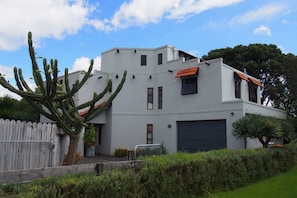 Una casa moderna de dos pisos con garaje, rodeada por una valla de madera y un gran cactus.