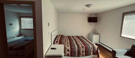 Un dormitorio con cama, mesita de noche, cómoda, televisor y ventana con persianas.