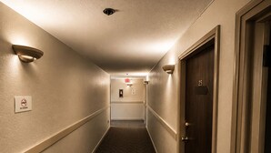Ein Hotelkorridor mit Teppichboden, Wandleuchten und einer Tür mit Nummernschild.