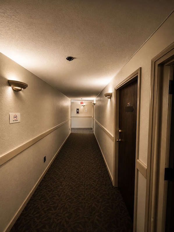 A hotel hallway with a carpeted floor, wall-mounted light fixtures, and a door with a number plate. - Clydesdale Inn (Surrey)