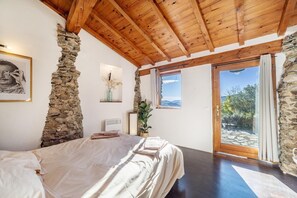 Une chambre à coucher avec un lit, des murs en pierre, des poutres en bois au plafond, une fenêtre et une vue sur l’extérieur.