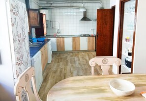 Een keuken met houten kastjes, een spoelbak en een eethoek met een tafel en stoelen.