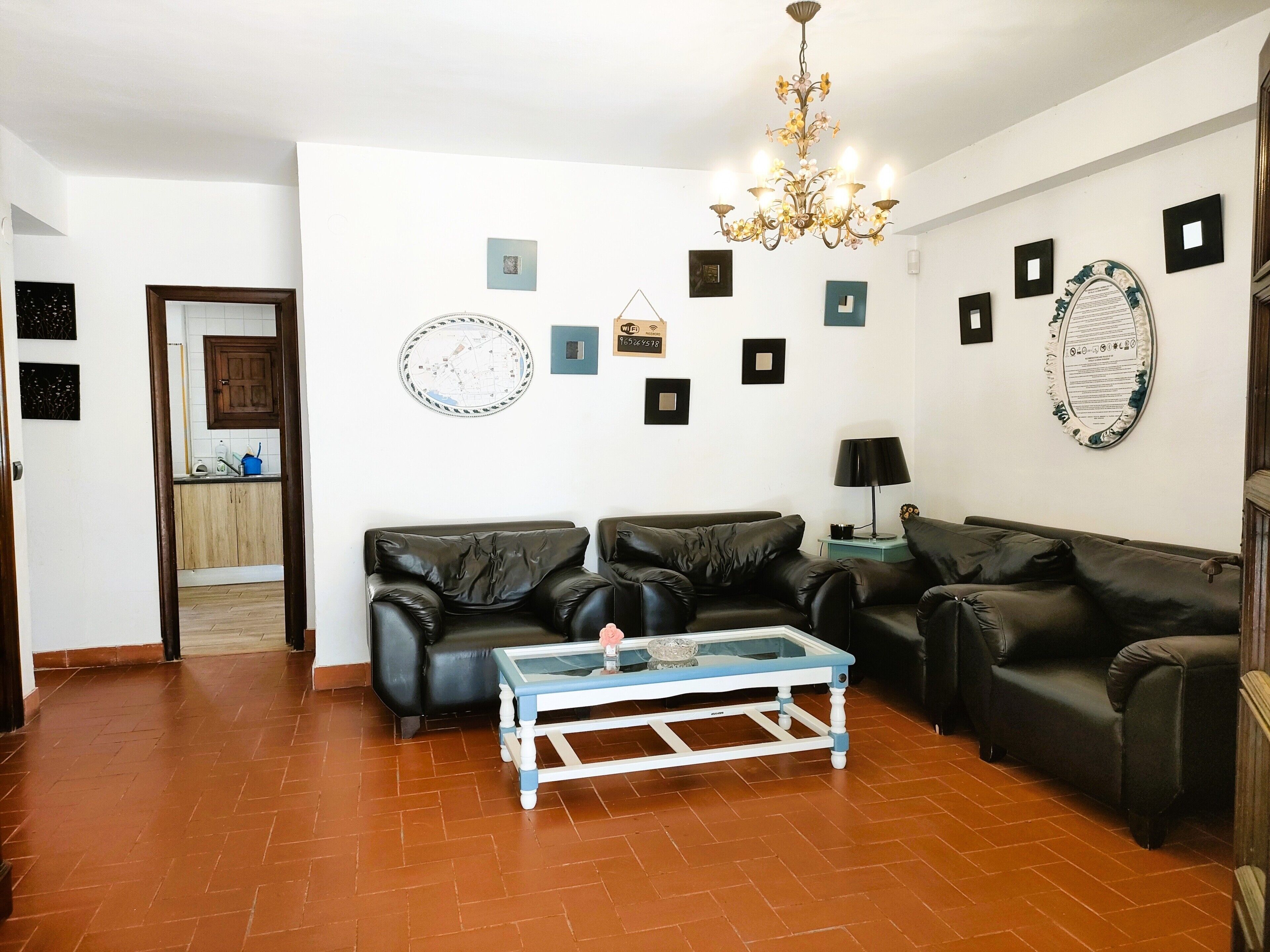 Una sala de estar con dos sofás de cuero negro, una mesa de centro de vidrio, una araña y varias fotografías enmarcadas en las paredes.