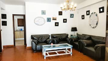 Una sala de estar con dos sofás de cuero negro, una mesa de centro de vidrio, una araña y varias fotografías enmarcadas en las paredes.