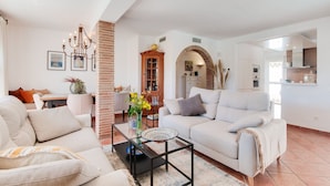 Un salon moderne avec un canapé, une table basse et un coin repas comprenant une table et des chaises. On aperçoit une cuisine au fond.