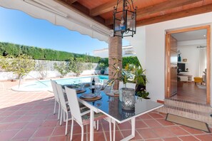 An outdoor dining area with a pool, white chairs, and a table set for dining.