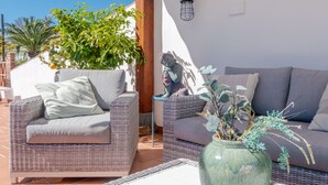 Une terrasse avec des meubles en osier, un vase vert contenant des plantes et une statue.