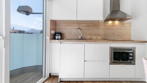 Une cuisine moderne avec des armoires blanches, une hotte de cuisinière en acier inoxydable, un four à micro-ondes encastré et une fenêtre donnant sur un paysage urbain.