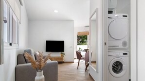 Un salon moderne comprenant un canapé, un téléviseur à écran plat, un coin repas avec des chaises et un lave-linge.
