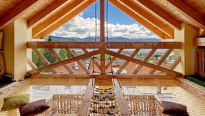 A high-ceilinged room with a wooden truss structure, a view of mountains, and a netted window sill.