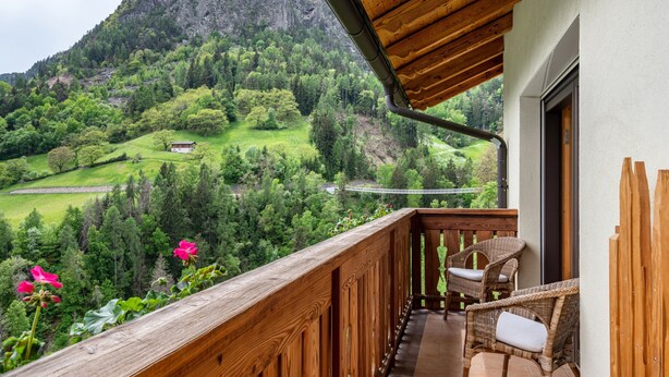 Un balcón con sillones de mimbre, vista a un valle verde y una montaña al fondo.