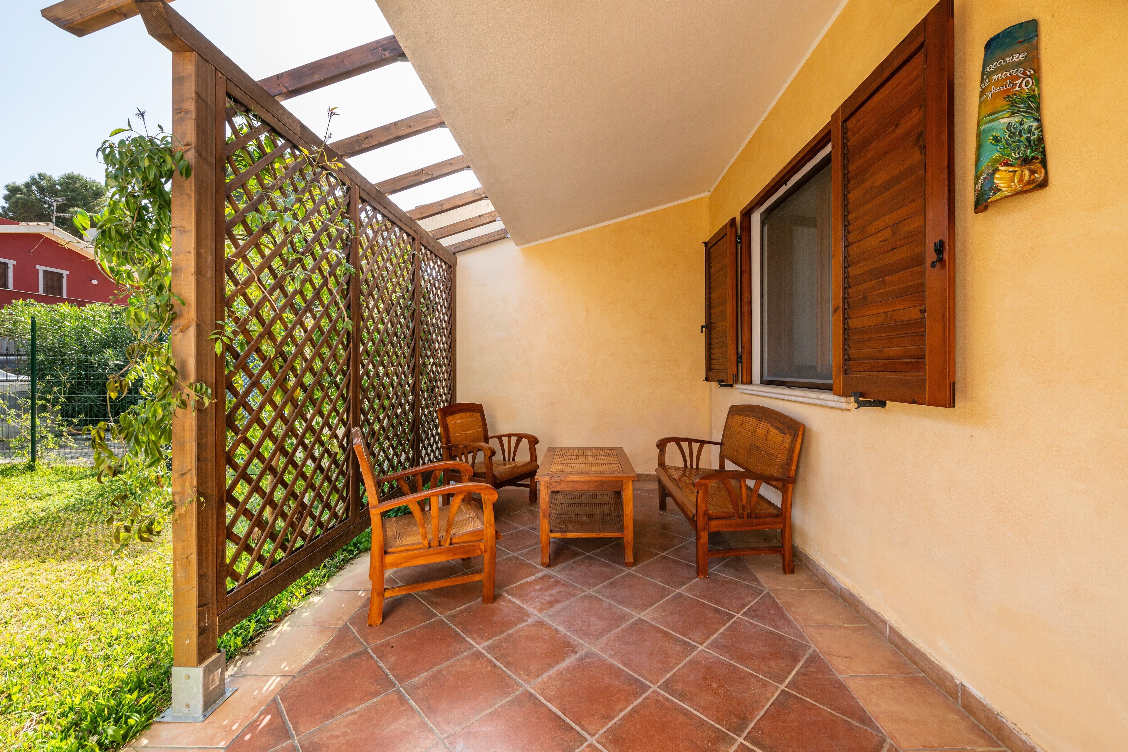 Un patio con mobiliario de madera, una celosía y una ventana con contraventanas.