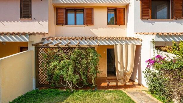 A two-story building with a covered patio, a wooden fence, and a small garden. - Holiday Home 'Sole E Mare' with Private Terrace, Private Garden and Air Conditioning (Porto Pino)