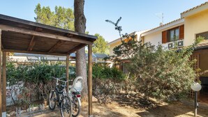 A covered outdoor area with a bicycle rack, a tree, and a building with a tiled roof. - Holiday Home 'Sole E Mare' with Private Terrace, Private Garden and Air Conditioning (Porto Pino)