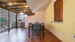 A dining area with a wooden table and chairs, a tiled floor, and a window with wooden shutters. - Holiday Home 'Sole E Mare' with Private Terrace, Private Garden and Air Conditioning (Porto Pino)