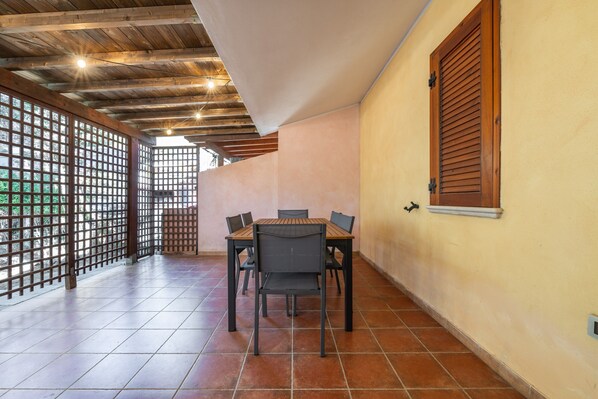 A dining area with a wooden table and chairs, a tiled floor, and a window with wooden shutters.