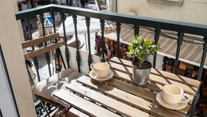 Un balcón con una mesa de madera, dos tazas blancas y una planta en maceta.