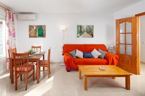 Una sala de estar con un sofá rojo, una mesa de comedor de madera, sillas y dos cuadros colgados en la pared.