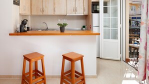 Una cocina con armarios de madera, un lavamanos, un microondas y una planta en maceta. Hay dos taburetes de madera y una puerta corrediza de vidrio que da a un espacio exterior.