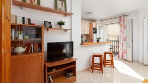 Una sala de estar moderna con televisor de pantalla plana, estanterías de madera y un comedor con balcón.